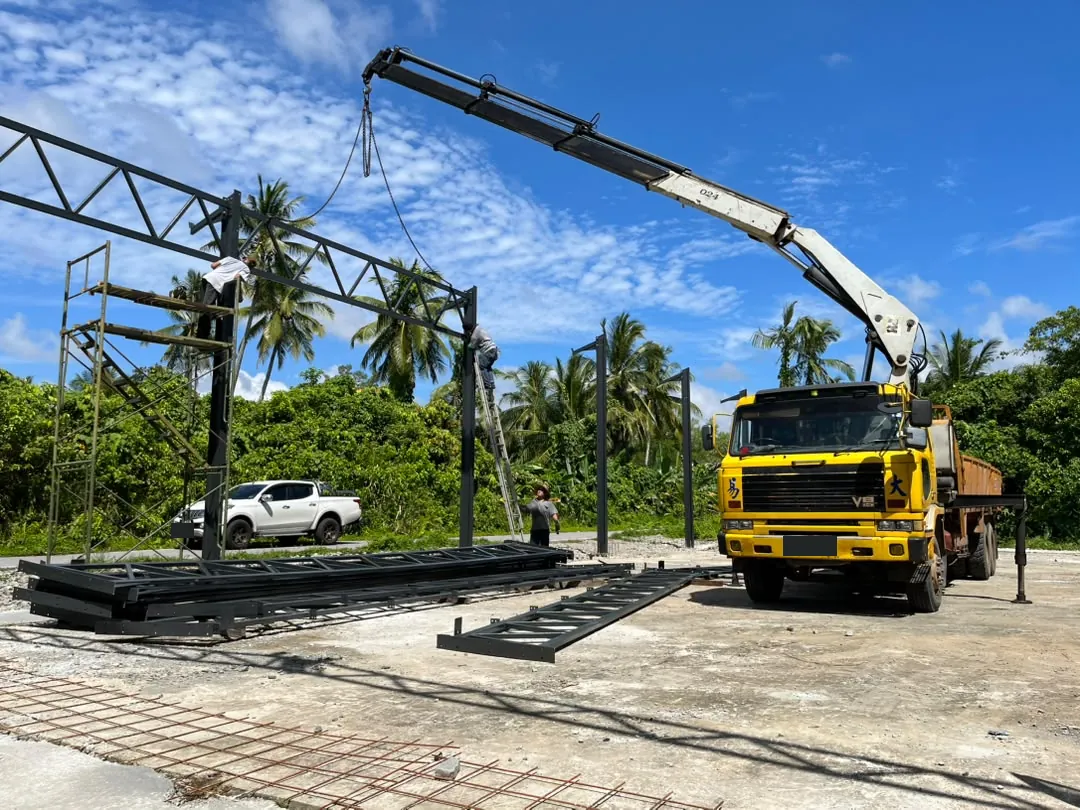 Yellow lorry mounted crane lifting a steel frame under a blue sky